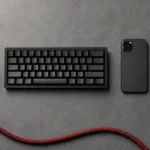 Which Semrush Plan Do You Need in 2026? Top-down flat lay of a console controller, mechanical keyboard, phone and laptop edge on a slate desk with a coiled red cable